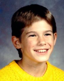 A young boy in a yellow sweater smiles for the camera.