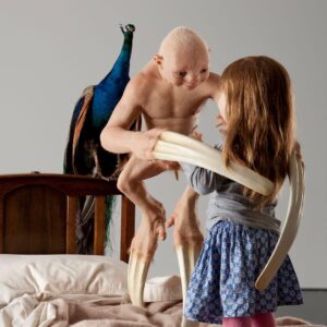 A little girl is playing with a peacock on a bed.