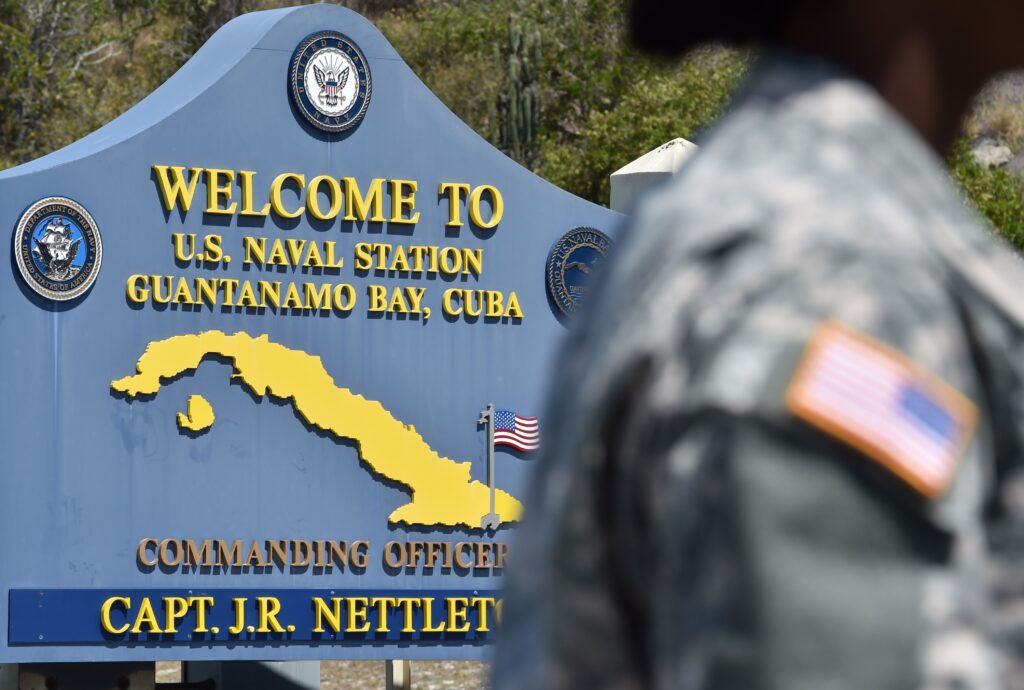 A soldier is standing in front of a sign that says welcome to guantanamo bay.
