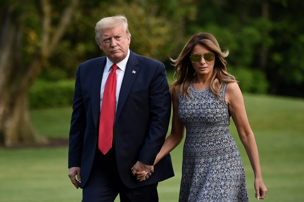 Donald trump and melania trump walk through a grassy field.