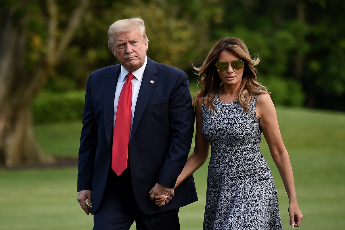 Donald trump and melania trump walk through a grassy field.