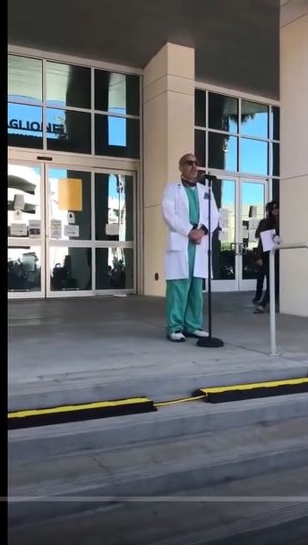 A man in a lab coat standing in front of a building.