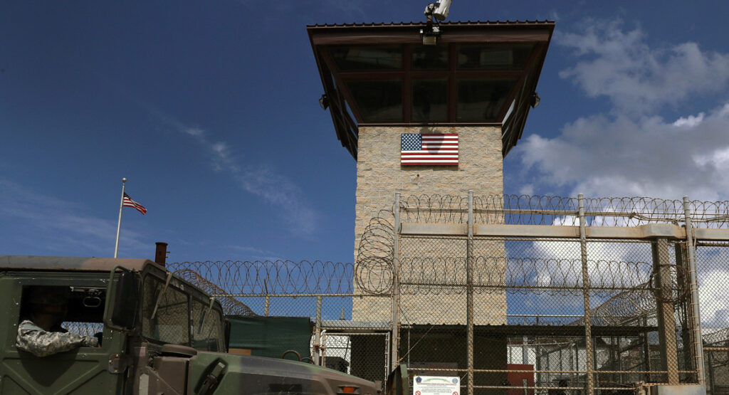 A military truck in front of a prison tower.