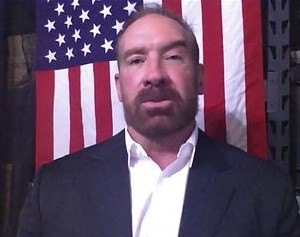 A man in a suit standing in front of an american flag.