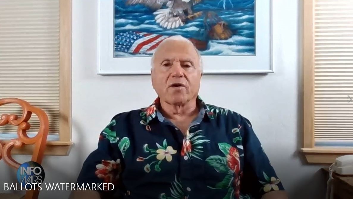 A man in a hawaiian shirt sitting in front of a desk.