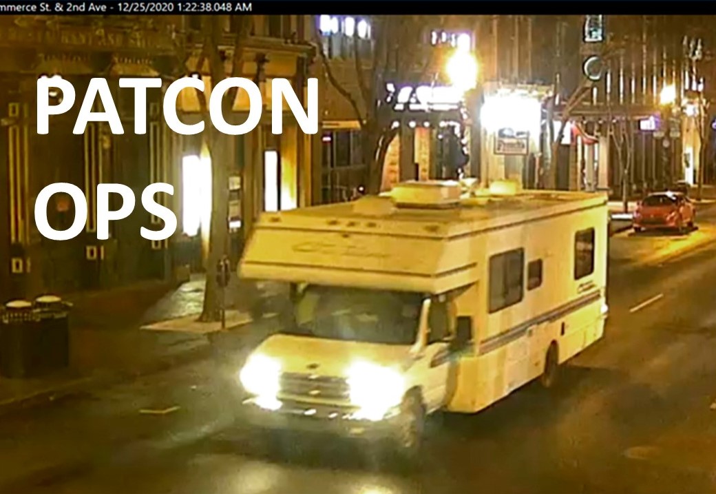 A white rv driving down a city street at night.