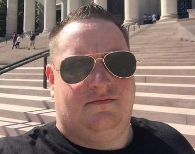 A man wearing sunglasses in front of a building.