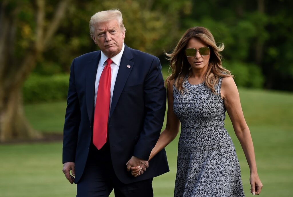 Donald trump and melania trump walk through a grassy field.