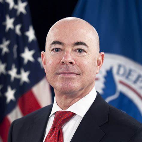 A bald man in a suit and tie standing in front of an american flag.