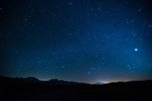 A night sky with stars and a mountain in the background.