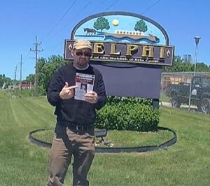 A person wearing a cap and standing holding a flyer  