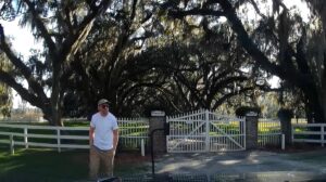 A man standing in front of a gate with spanish moss.