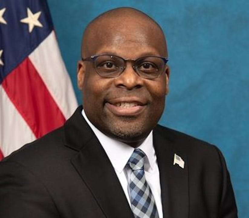 A black man in a suit and tie standing in front of an american flag.