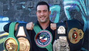 A man holding two boxing belts in front of a graffiti wall.