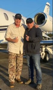 Two men standing in front of a private jet.