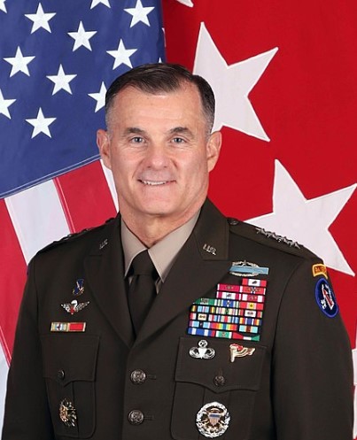 A man in a military uniform standing in front of an american flag.