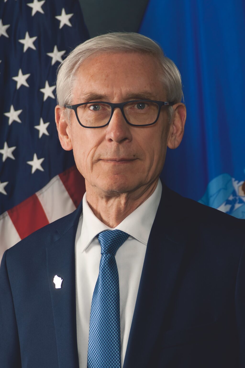 A man in a suit and tie standing in front of flags.