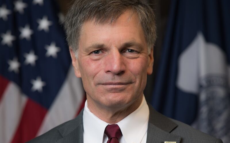 A man in a suit and tie in front of flags.